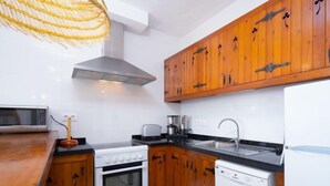 A modern kitchen with wooden cabinets, a stainless steel range hood, a microwave, a stove, a coffee maker, and a dishwasher. - Pueblo de la Luz by Interhome (Benitachell)