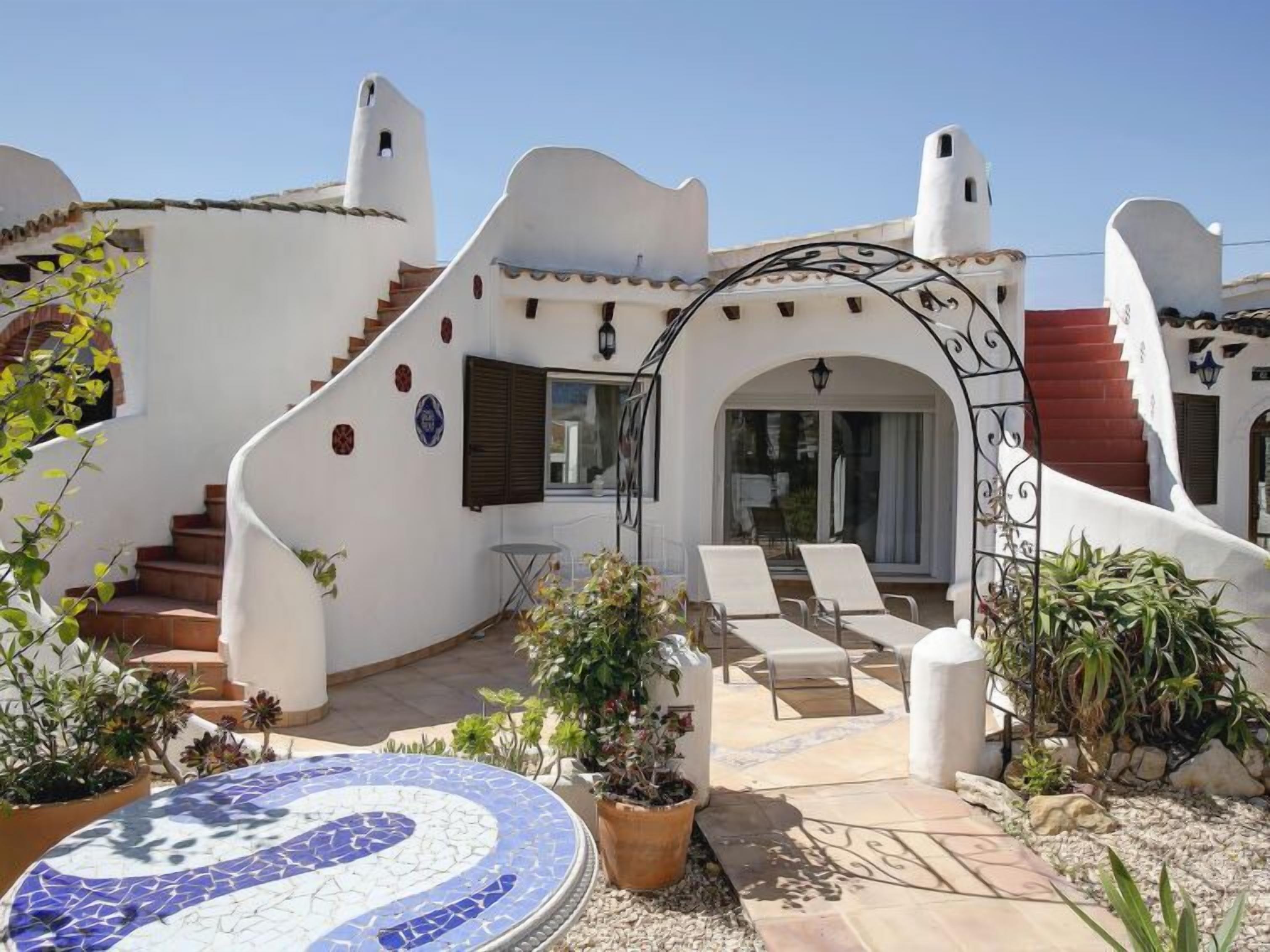 Um edifício branco com escadaria curva, área de estar externa e um pátio com azulejos.