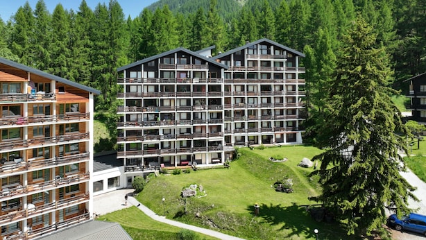 Un hotel a più piani con balconi, immerso nel verde e con vista sulle montagne.