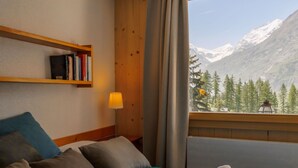 Una camera d'albergo con un letto, cuscini, una lampada, una libreria e una finestra vista montagna.