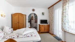 A bedroom with a bed, wooden wardrobe, TV, and a window with curtains. - Dachstein Top 27 by Interhome (Flachau)