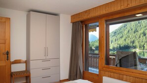 A bedroom with a bed, a wardrobe, a chair, and a window with a view of a forested mountain. - Parc C013 by Interhome (Champex)