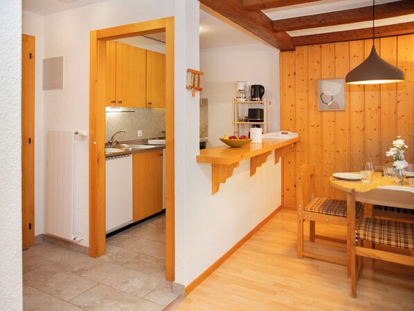 A compact kitchen with wooden cabinets, a built-in oven, and a small dining area with a table and chairs.