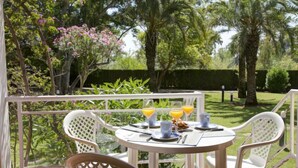 A round table with chairs on a balcony, surrounded by lush greenery and palm trees. - Apartment Keops by Interhome (Oliva)