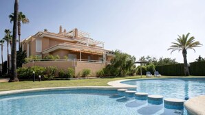 A swimming pool with a curved edge and a series of steps leading into it, surrounded by a well-maintained lawn and palm trees. - Apartment Keops by Interhome (Oliva)