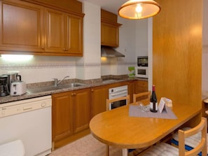 A compact kitchen with wooden cabinets, a granite countertop, a built-in oven, a microwave, and a small dining table with chairs.