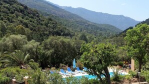 Zona de piscina rodeada de abundante vegetación y montañas al fondo.