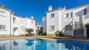 A pool area with white buildings, a clear blue sky, and a staircase leading to a balcony. - Club Sevilla I by Interhome (Oliva)