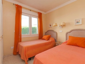 A bedroom with two beds, a window with curtains, bedside lamps, and a wall-mounted light fixture.