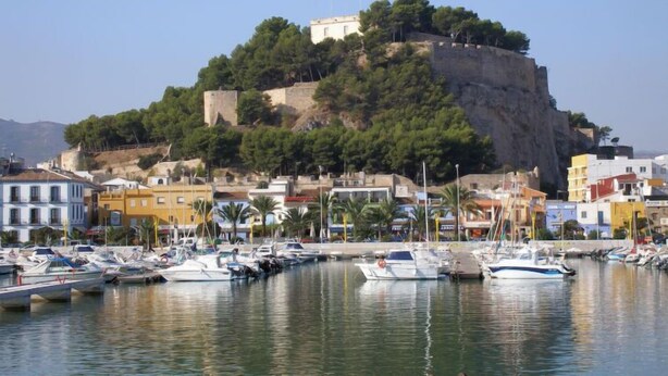 A coastal town with a historic fort on a hill, marina with boats, and colorful buildings. - Club Sevilla I by Interhome (Oliva)