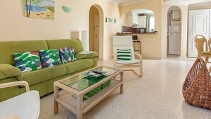 A living room with a green sofa, a glass coffee table, and a wicker chair. - Club Sevilla I by Interhome (Oliva)