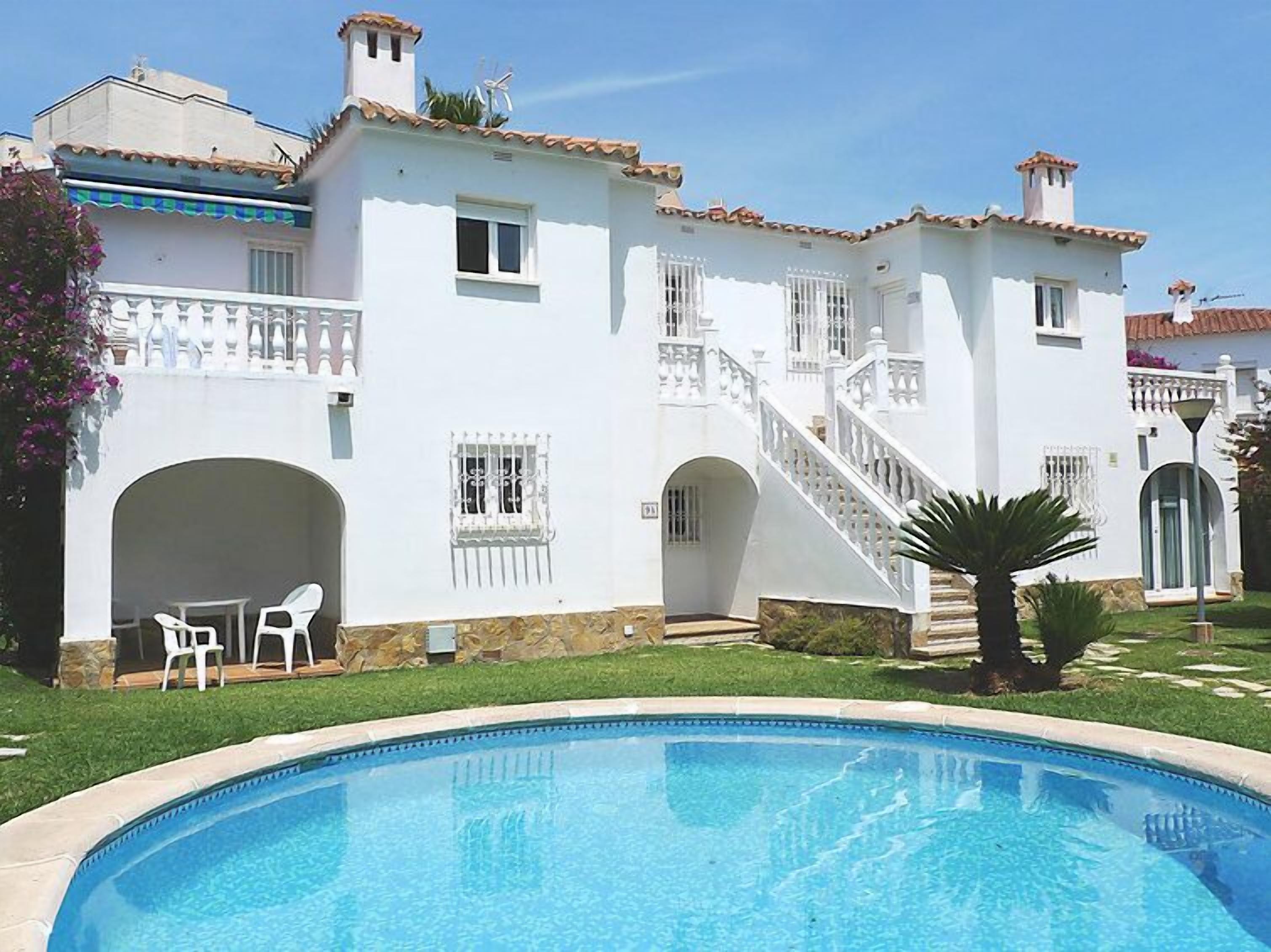 Un edificio blanco con piscina, una escalera y un pequeño patio con sillas.