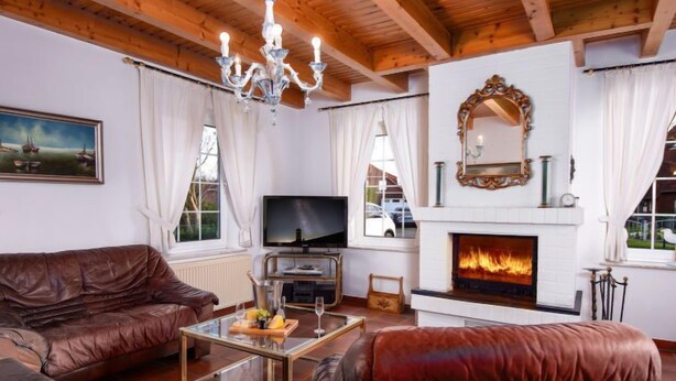 Una sala de estar acogedora con chimenea, sofás de cuero, una mesa de centro de vidrio y una araña.