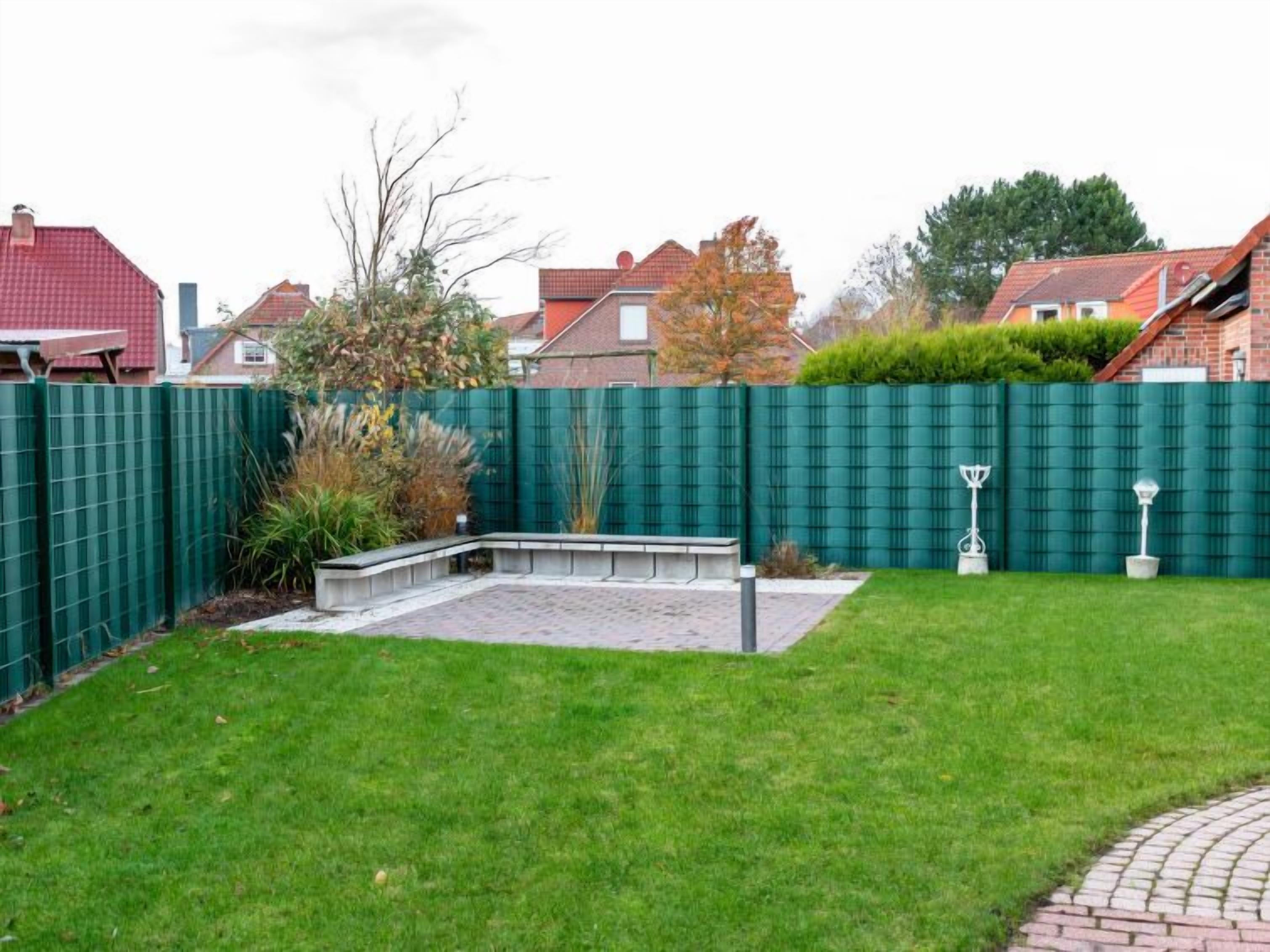 A residential backyard with a green fence, a paved patio area, and a well-maintained lawn.