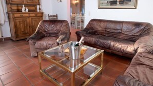 Un salón con sofás de cuero, una mesa de centro de vidrio, armarios de madera y un cuadro con barcos de vela.