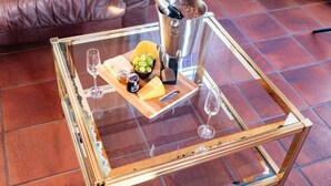 Una mesa con cubierta de vidrio, una botella de champán, un bol de uvas, una rebanada de queso y un cuchillo.