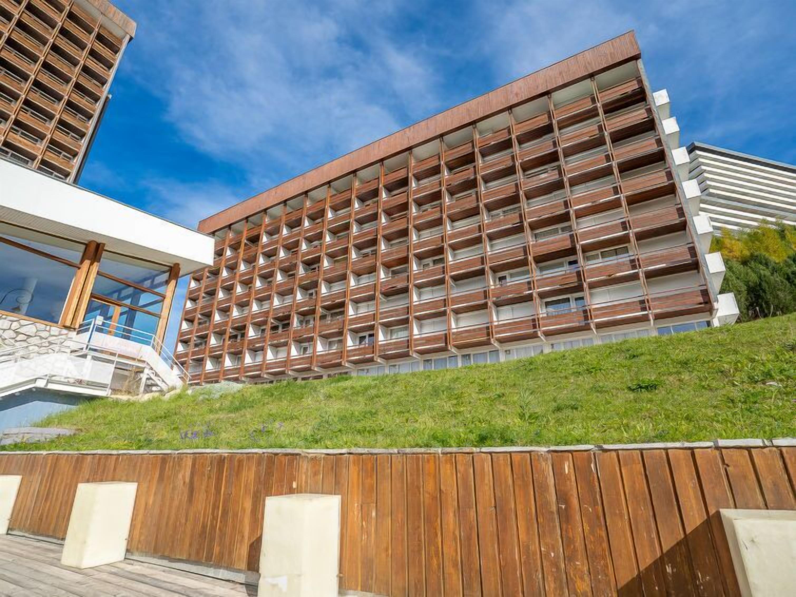 A modern building with a multi-story structure, featuring a series of balconies and a wooden facade.