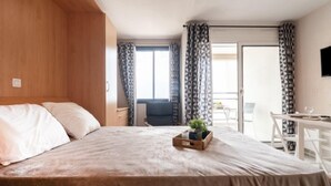 A hotel room with a bed, a small table with a plant, a chair, and a balcony with curtains. - Apartment Casino by Interhome (Canet-Plage)