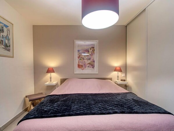 A bedroom with a bed, two bedside tables, a nightstand, a bench, a ceiling light, and a framed picture on the wall.