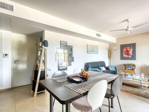 A modern living room with a dining area, featuring a sofa, chairs, a coffee table, and a ceiling fan.