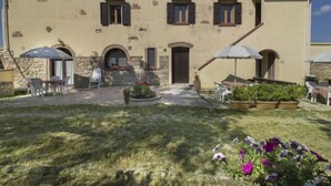 Un bâtiment doté d’une façade en pierre, de nombreuses fenêtres et d’une petite cour intérieure aménagée avec des sièges et des plantes en pot.