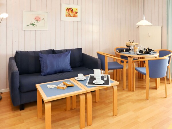 Una habitación acogedora con un sofá azul oscuro, una mesa de comedor de madera con sillas y una pequeña mesa auxiliar con libros y una taza.