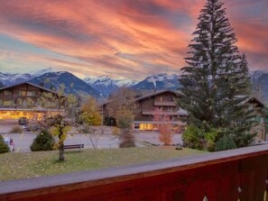 Un albergue de montaña con varias construcciones, un área de estacionamiento y vistas a montañas nevadas bajo un cielo colorido.
