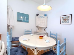 Un comedor con una mesa redonda, sillas azules y un armario blanco con un reloj encima.