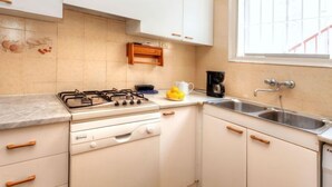 A kitchen with white cabinets, a gas stove, a coffee maker, and a window with a view. - Nicolas by Interhome (Llançà)