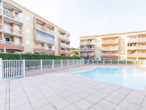 A modern apartment building with a swimming pool, balconies, and a white fence.
