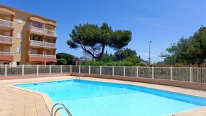 Une piscine entourée d’une clôture blanche, un ciel bleu dégagé et, au loin, un immeuble à plusieurs étages.