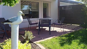 Un patio con mesa y sillas, una escultura de pájaro y una casa con toldo rojo y blanco.
