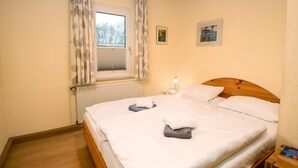 Una cama bien hecha con ropa blanca y una toalla gris, una lámpara de noche y un cuadro en la pared.