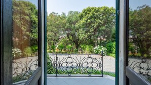 A view through a window with a decorative iron railing, leading to a garden with trees and a gravel path. - Bagnolo by Interhome (Albisola)