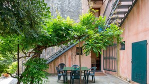 A stone patio with a table and chairs, surrounded by greenery and a building with a staircase. - Bagnolo by Interhome (Albisola)
