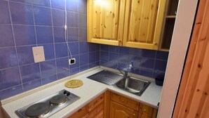 Una cocina con azulejos azules, armarios de madera, un lavamanos de acero inoxidable y una estufa.