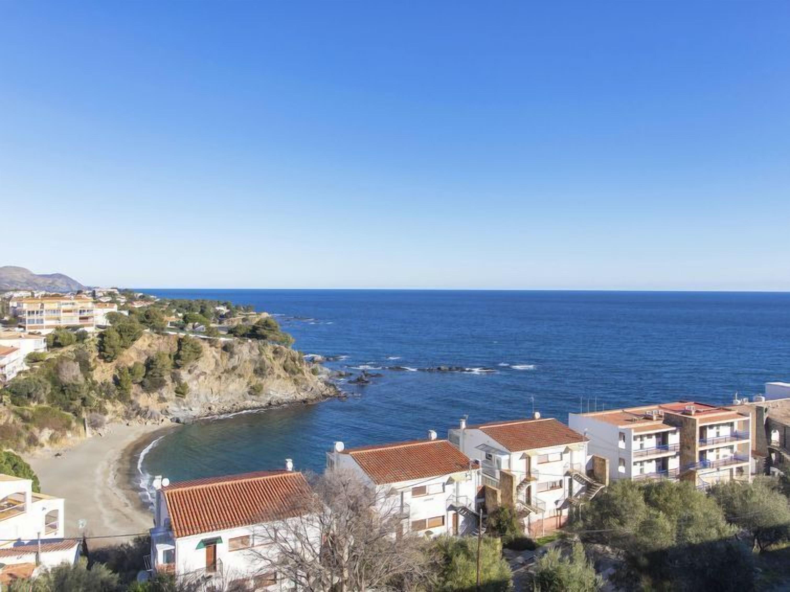 A coastal town with buildings along the shoreline, a clear blue sky, and a view of the sea.