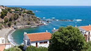 Une vue côtière comprenant une plage, des falaises rocheuses et des bâtiments aux toits recouverts de tuiles rouges.