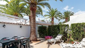 Eine Terrasse mit Esstisch, Lounge-Sesseln und einer Palme.