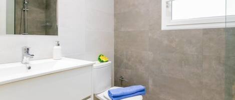 A modern bathroom with a white sink, a mirror, a shower, and a toilet.