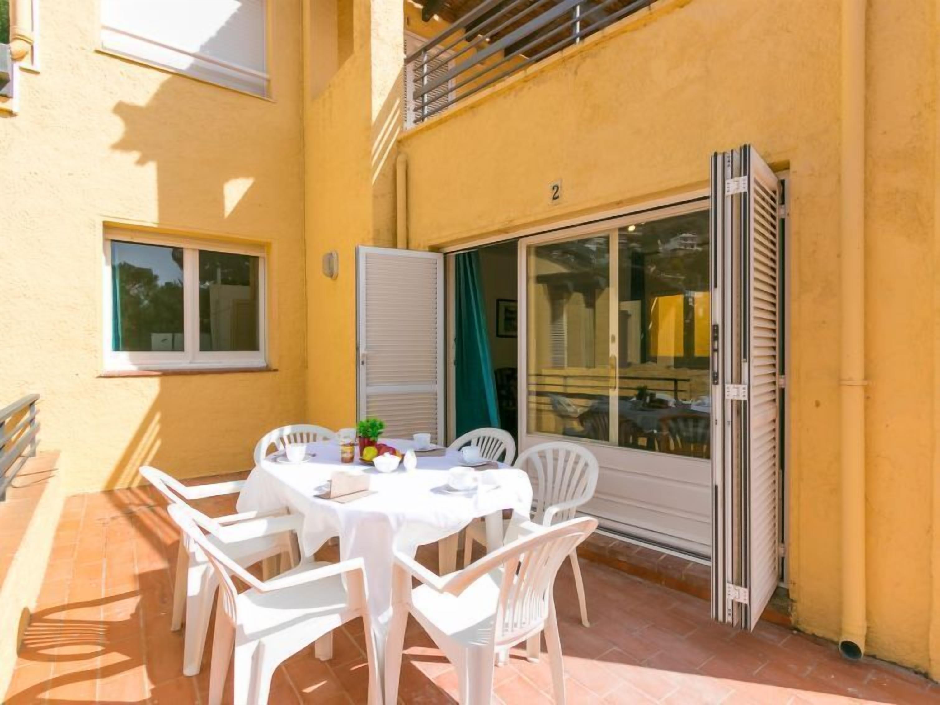 An outdoor patio with a table set for four, surrounded by white chairs.