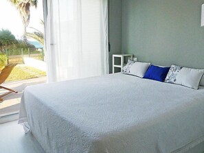 A bedroom with a large bed, a small bedside table, and a view of a garden through a window.