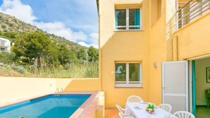 Zona junto a la piscina con piscina, sillas blancas y una mesa dispuesta para comer.