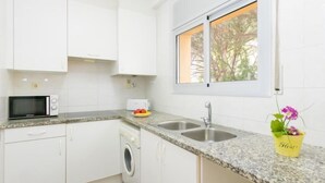Una cocina moderna con armarios blancos, microondas, lavadora, encimeras de granito, un fregadero y una ventana con vistas a árboles.