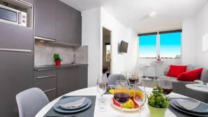 A modern dining area with a round table set for four, a kitchen with grey cabinets, and a view of the sky through a window. - Port Mistral by Interhome (Empuriabrava)