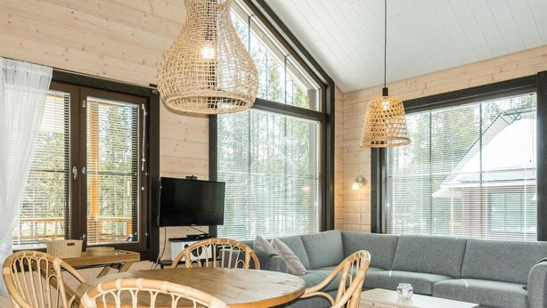 Un salon chaleureux avec un canapé gris, une table à manger en bois entourée de chaises et un téléviseur posé sur un meuble.