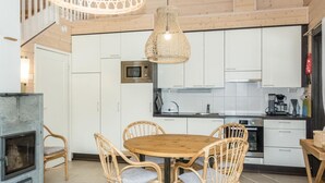 Une cuisine moderne avec des meubles blancs, un four à micro-ondes, une cuisinière et un coin repas comprenant des chaises en osier et une table en bois.