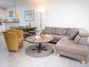 A modern living room with a beige sofa, a yellow armchair, and a round coffee table with decorative items.