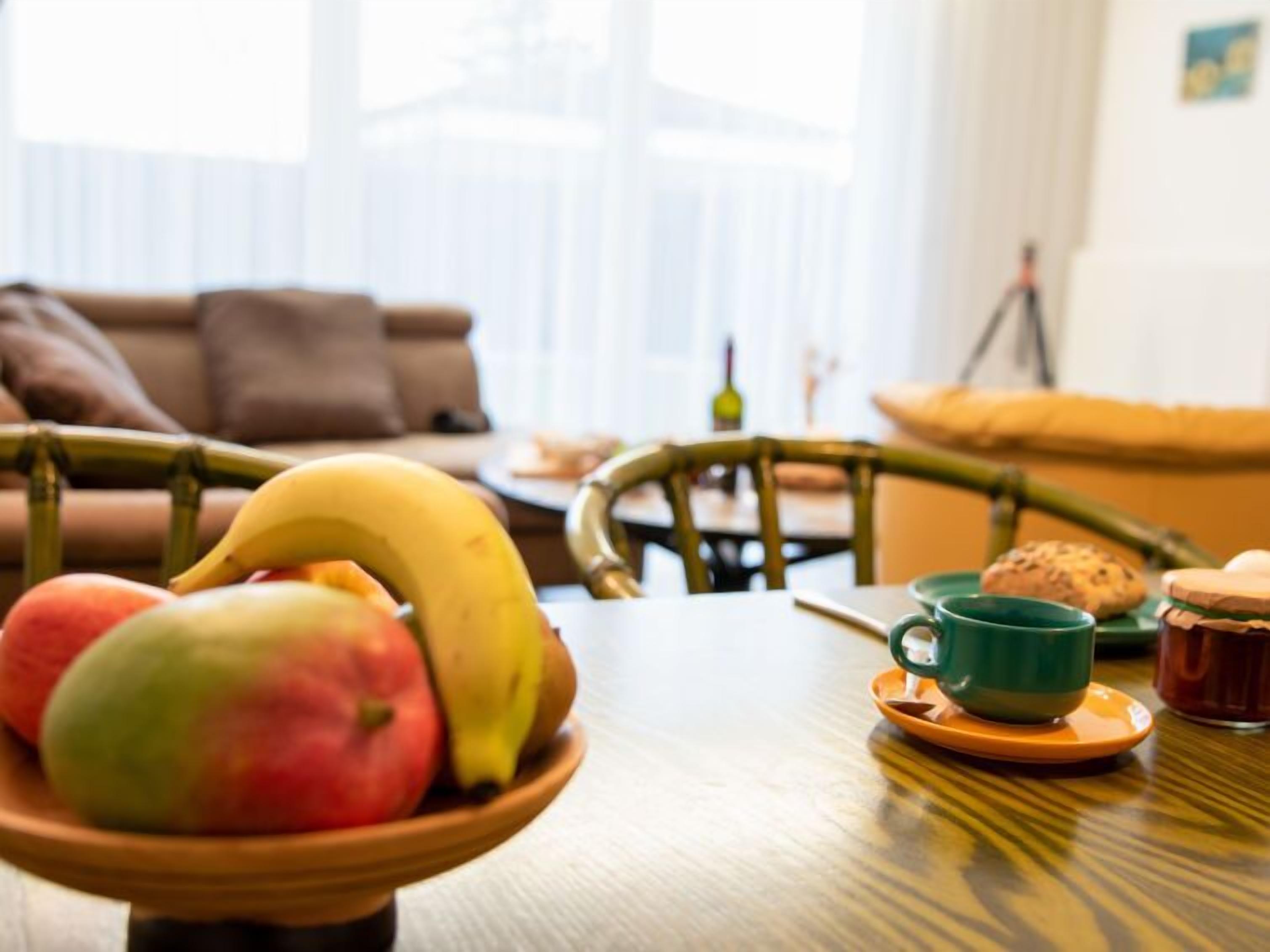 Une table à manger avec un saladier de fruits, une tasse verte et un pot de confiture.