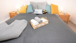 A neatly made bed with a grey quilt, a grey knitted blanket, and a wicker basket with rolled towels. - Vacation home Butzel by Interhome (Norddeich)